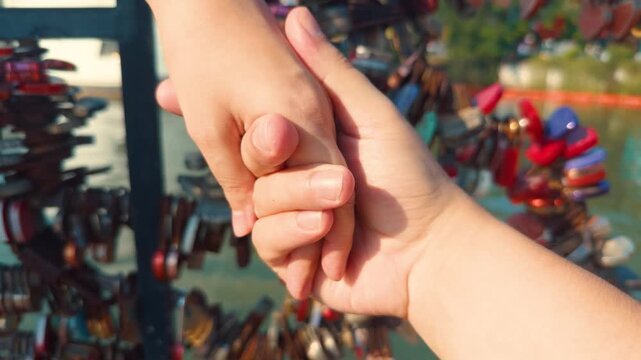 Couple's hands intertwined, representing romantic partnership, intimacy, and a journey together, with a background of colorful love padlocks symbolizing unbreakable bonds and shared memories