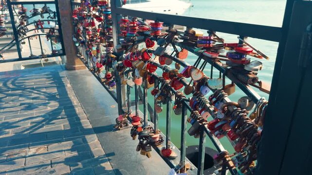 Heart and traditional padlocks in varied colors fastened to a metal bridge railing, symbolizing enduring love, travel memories, promises and romantic commitment by the waterfront