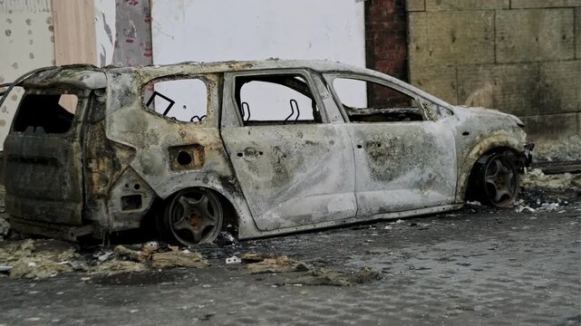 Burned out car wreck abandoned on city street. Destroyed vehicle after fire accident. Vehicle hulk as result of war conflict or arson. Urban catastrophe and property damage concept.