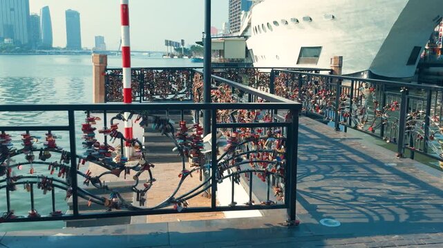 Hundreds of colorful padlocks representing eternal love and commitment decorating the railings of the love locks bridge in da nang, vietnam, with a cruise ship and city skyline in the background