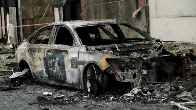 Burned out car wreck abandoned on city street. Destroyed vehicle after fire accident. Vehicle hulk as result of war conflict or arson. Urban catastrophe and property damage concept.