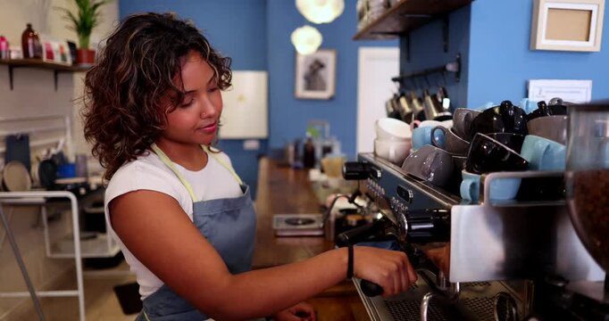Young female employee preparing a hot beverage with a professional machine in a cafeteria. She is focused on her work, handling the portafilter and ensuring a quality coffee making process