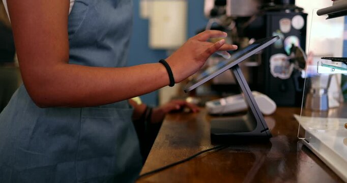 Unrecognizable african american female barista wearing an apron entering an order on a point of sale touchscreen tablet, managing transactions and serving customers in a modern coffee shop