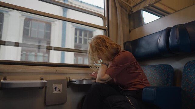 Pensive woman with blonde hair sitting alone in a train compartment, looking out the window while traveling. Atmospheric journey with a nostalgic feeling