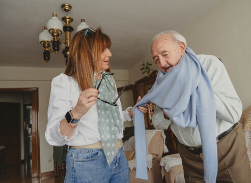 Daughter helping senior father with scarf at home