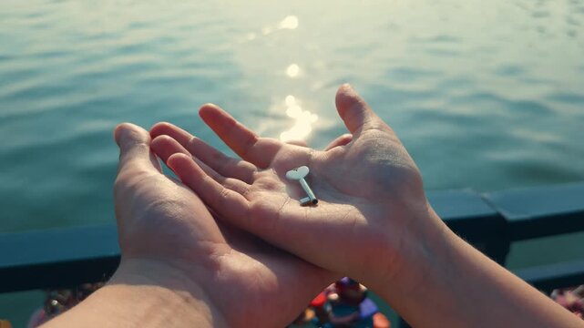 Person's hands gently holding a tiny heart key, representing finding the answer to a problem, unlocking potential, or signifying a precious relationship over sparkling blue water