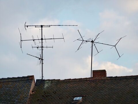 Old roof with antenna array. Rusty metal antennas atop aged tile roofing against overcast sky