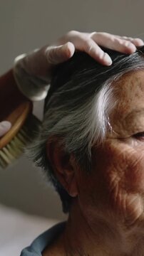 Vertical video: Bringing wood brush gloved aide brushing senior right hair in bed for care blue top