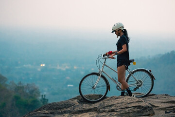 Fototapeta premium Female cyclist mountain bike rocky cliff safety helmet outdoor sport active lifestyle sunset light mountain view adventure travel nature landscape Confident female cyclist with mountain bike rocky