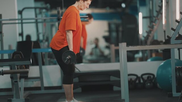 Elderly woman performing barbell romanian deadlifts in the gym