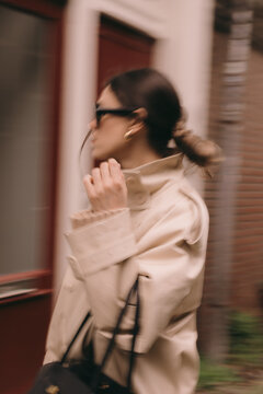 Close-up artistic motion blur of a stylish woman with a messy bun and gold earrings walking past a brick building, urban fashion lifestyle, cinematic movement effect, modern aesthetic