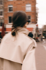 Obraz premium Blurred artistic portrait of a stylish woman in a beige trench coat walking down a European city street with motion blur effect dynamic urban lifestyle cinematic out of focus street fashion aesthetic