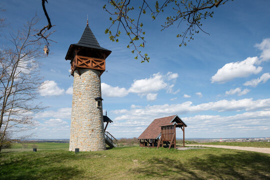 Scenic stone lookout tower with a wooden gallery on a grassy hill under a bright blue sky with white clouds, Holic, Slovakia