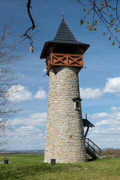 Scenic stone lookout tower on a grassy hill under a bright blue sky with white clouds, Holic, Slovakia