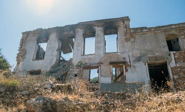 Abandoned stone house ruins under bright summer sunlight in rural hillside landscape
