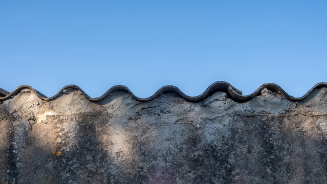 Weathered concrete wall with wavy corrugated top under blue summer sky