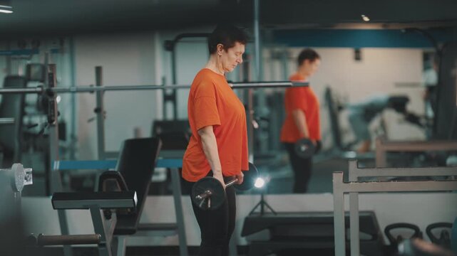 Senior woman performing barbell rows at the gym