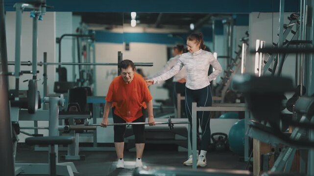 Personal trainer instructing senior woman lifting barbell in gym