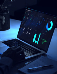 Man working late night at desk analyzing financial trading charts on laptop screen with energy...