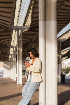 Young woman smiling while engaging with her smartphone in an outdoor urban setting