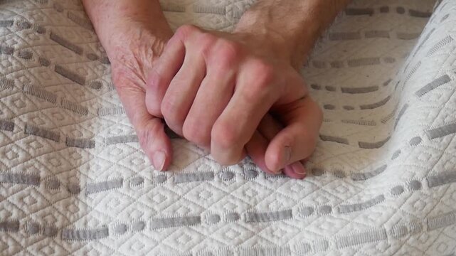 A young man places his hand on the hand of an elderly woman next to him