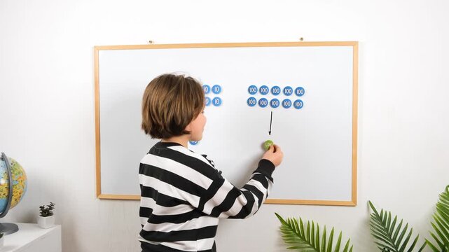 Young boy learning arithmetic with magnetic numbers and place value labels. STEM education concept showing logical thinking, problem solving, and cognitive development.