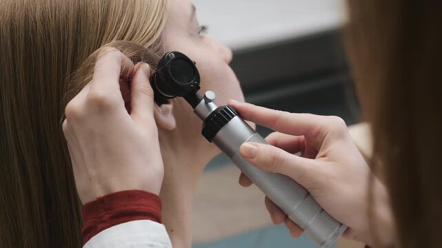 Doctor performing ear examination with otoscope in clinic close up diagnostic procedure otolaryngology check healthcare indoors.