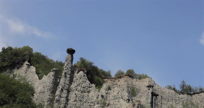 Zone earth pyramids above Lake Iseo Lombardy Italy, arc pan left to right follows sandy cliffs and hoodoo columns from small spires to a towering boulder capstone