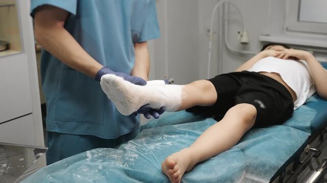 Doctor shaping and adjusting plaster cast on child leg in clinic finalizing immobilization and ensuring proper fit orthopedic treatment process trauma care indoors.