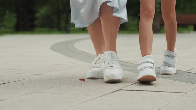 Mother and daughter strolling outdoors. Footsteps of mom and daughter on park pavement during daylight. Relaxed summer day scene showing mother and daughter enjoying outdoor walk together