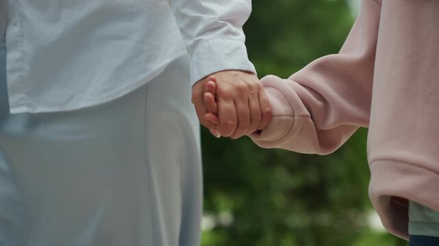 Mother and daughter outdoors. Walking hand in hand together. Mother guides child safely along shaded garden pathway. Calm mother and daughter enjoy protective walk on lush scenic trail