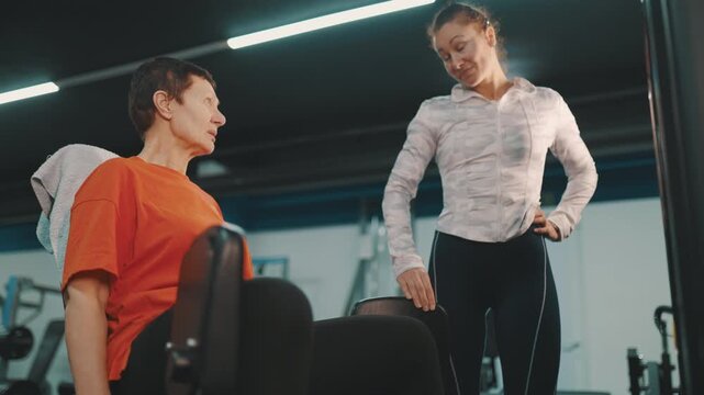 Personal fitness trainer coaching senior woman on leg extension machine