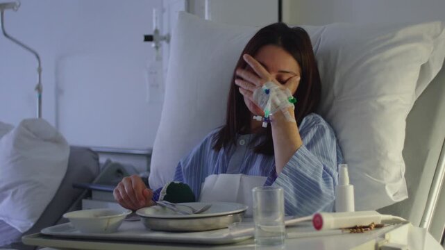 Female patient in hospital bed touching face with intravenous line in hand, eyes closed in fatigue, conveying discomfort, emotional strain, recovery and physical weakness