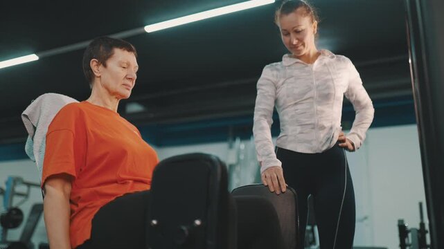 Personal trainer guiding senior woman on leg extension machine