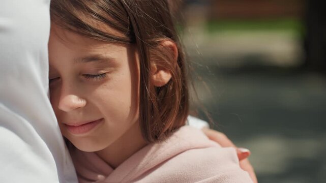 Girl shares tender maternal embrace. Child warmly embraces his mother as they enjoy tranquil park moments. Young girl and her mother share affectionate hug during calm outdoor setting in park