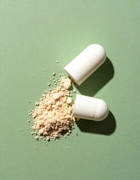 Open white medicine capsule with spilled powder on a green background