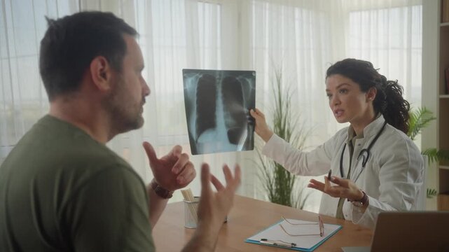 Caucasian female doctor showing chest x-ray image to male patient and explaining diagnosis during checkup in clinic