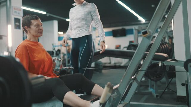 Personal trainer assisting senior woman on seated cable row machine