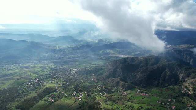A flight and a view from the cockpit through low-hanging clouds. The fog lifts over the Aspromonte National Park in southern Italy, revealing winding mountain roads.