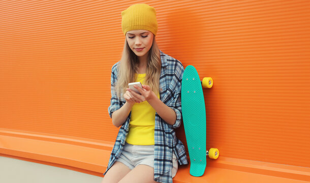 Modern young woman using smartphone, stylish teenage girl holding mobile phone with skateboard
