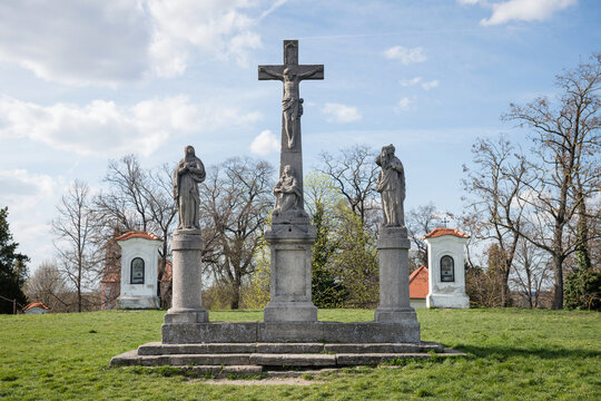 The Calvary in Skalica, Slovakia, featuring stone sculptures of the Crucifixion and white stations of the cross on a grassy hill under a blue sky
