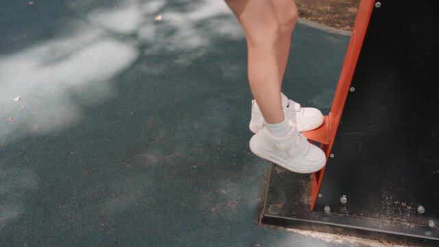 Closeup white daughter testing jump on playground step, denim shorts and white sneakers, rubber safety surface, dappled sunlight and shadow, slight hesitation then confident push, playful summer