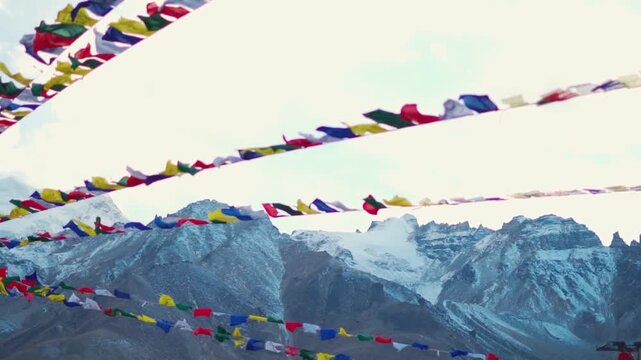 Defocused colorful Buddhist prayer flags waving in the wind in front of snowy Himalayan mountain peaks during the autumn season as seen from Padum town in Zanskar region of Ladakh, India.