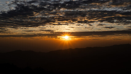 Obraz premium Majestic Golden Sunburst Breaking Through Dramatic Clouds over Mountain Silhouettes at Sunrise