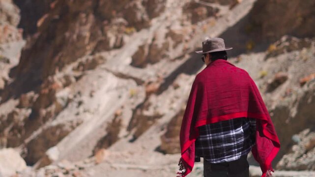 Rear view shot of an Indian male tourist walking on a hiking trail besides blue colored Tsarap river in front of rocky Himalayan mountains as seen during trek towards Phugtal Monastery in Zanskar.