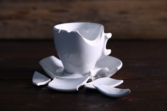 Broken ceramic cup and saucer on wooden table, closeup