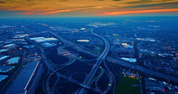 Stunning large modern interchange in the vast cityscape. Overcast orange sky over the misty city scenery at sunset time. Aerial view.