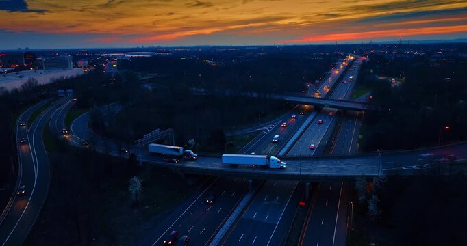 Cars with headlights switched on go by the motorways and trestles at dusk time. Striking orange sky in the backdrop.