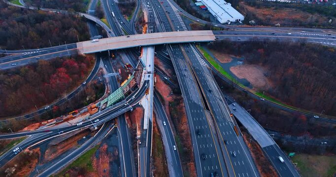 Vehicles go to diverse sides by the motorways of the interchange. Wooded areas are along the roads. Aerial view.
