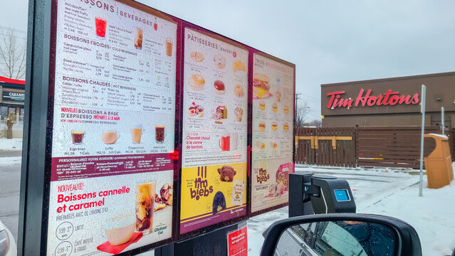 Tim Hortons drive-thru menu board displaying beverages and pastries in frozen rain setting with a car in the foreground